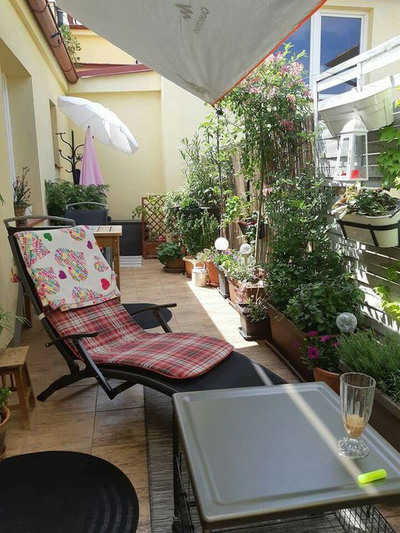 a balcony with planters, flowers and a trellis with green plants, a lounger with cushions, side tables and stools