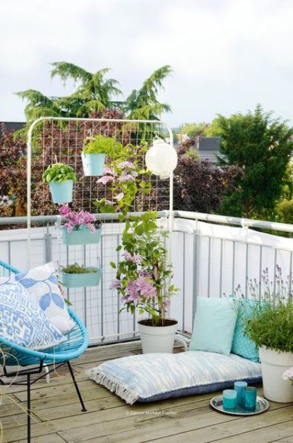 a balcony with some colorful furniture, accessories and cushions, potted plants, a screen with planters and some climbing vines
