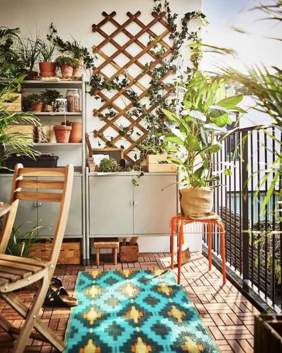a bright balcony with gray storage and shelving units, a trellis of greenery, potted plants, folding furniture and a statement rug