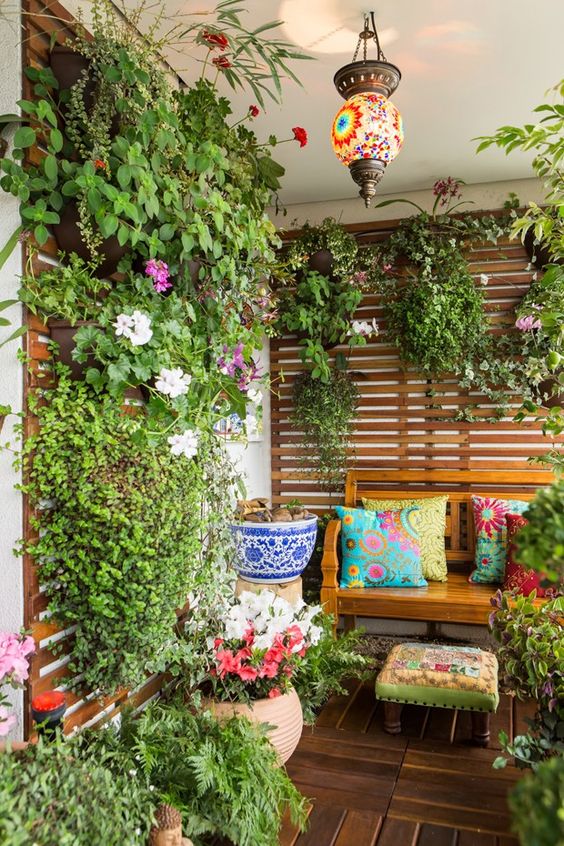 a bright boho balcony with a wooden bench, a trellis with green plants and flowers and another matching, colorful boho lamp