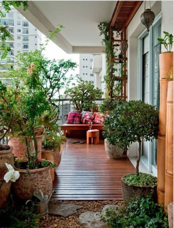 a modern balcony with wooden floors and some stones, potted plants, a corner sofa with cushions, a trellis with green plants