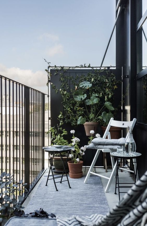 A Scandinavian balcony with folding furniture, a trellis with vines and planters with greenery and flowers is a very chic space