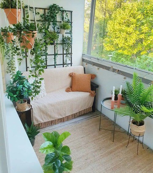a small and cozy balcony with a love seat, some cushions, side tables, a rug, potted plants and a trellis with vines and plants attached