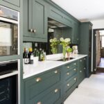 an elegant hunter green kitchen with white countertops, a mirror .