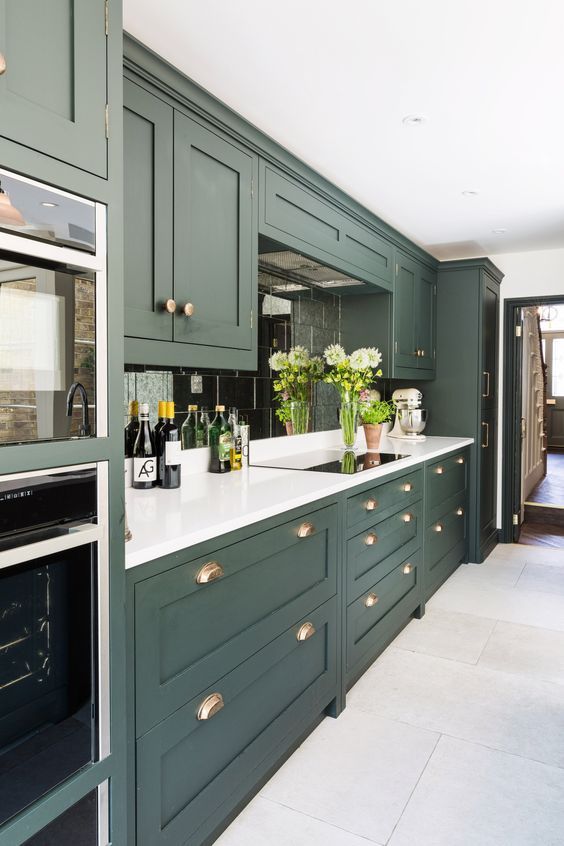 an elegant hunter green kitchen with white countertops, a mirror .