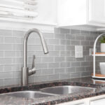 A kitchen sink detail shot with white cabinets, grey subway tile .