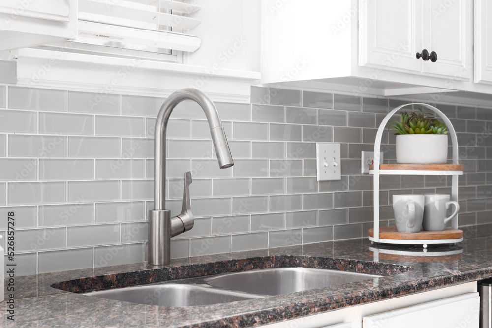 A kitchen sink detail shot with white cabinets, grey subway tile .