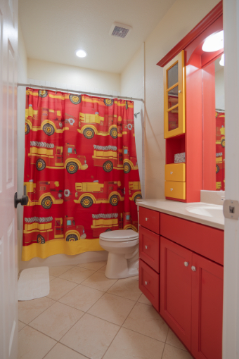 A small bathroom with red cabinets and a red and yellow truck-style shower curtain.