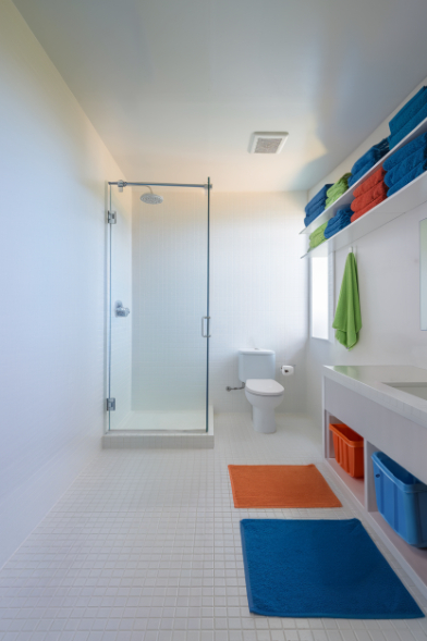 Modern bathroom with glass shower, white tiles and colorful towels on shelves.