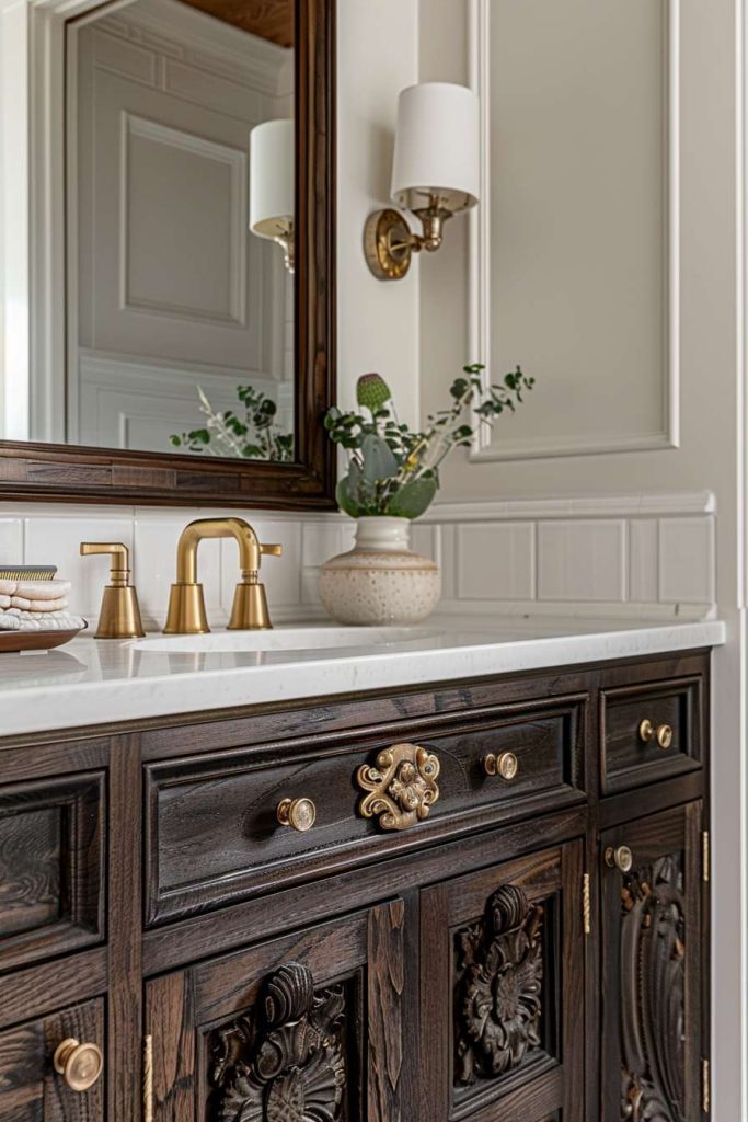 Bathroom vanity with ornate dark wood cabinets, a white countertop, a brass faucet and a sconce. There is a potted plant and a decorative tray on the counter.