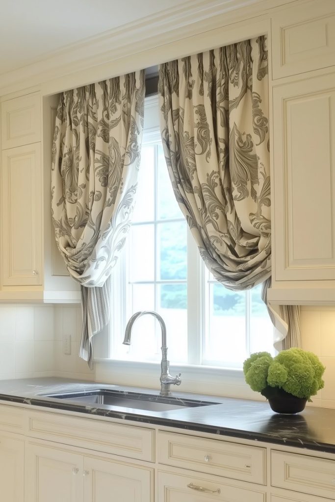 There is a kitchen sink with a silver faucet under a window. Patterned curtains frame the window and a green plant sits on the black countertop. Cream-colored cabinets surround the area.