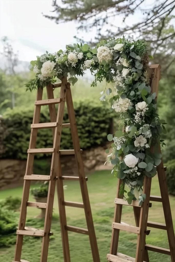 Two wooden ladders form a floral arch with white and green flowers in a garden setting.