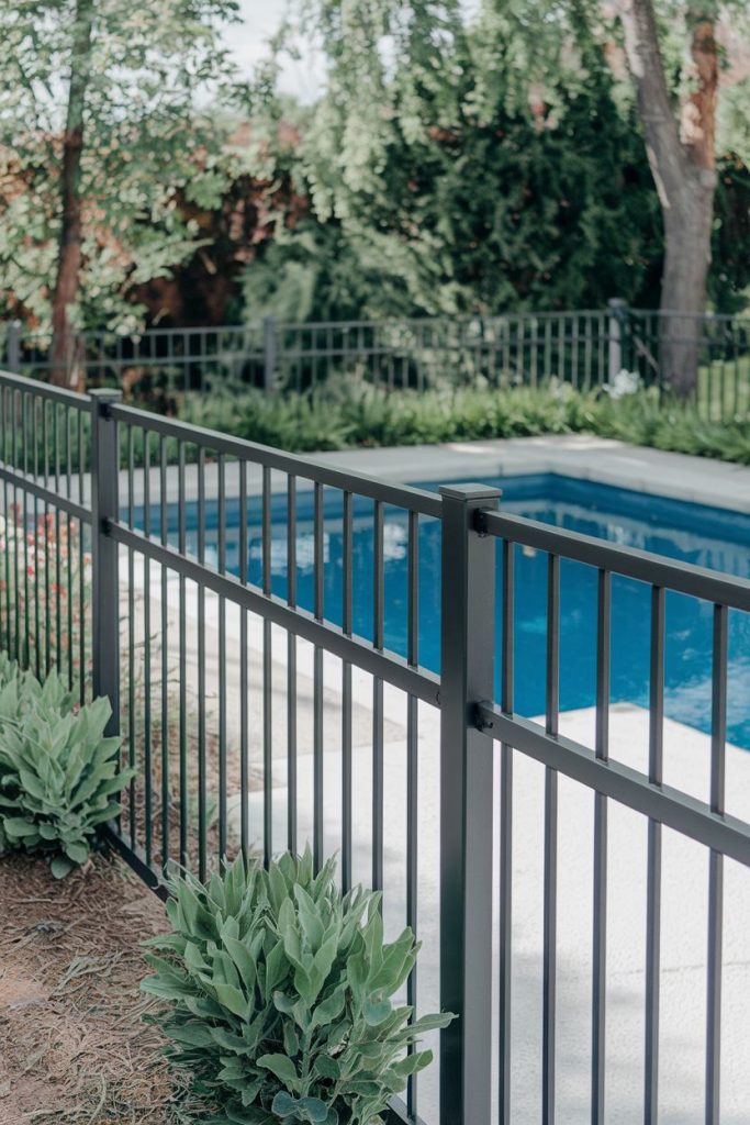 A black metal fence surrounds an outdoor pool with lush greenery.