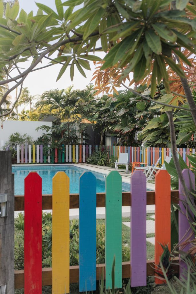 Colorful fence in front of a pool surrounded by tropical plants and trees.