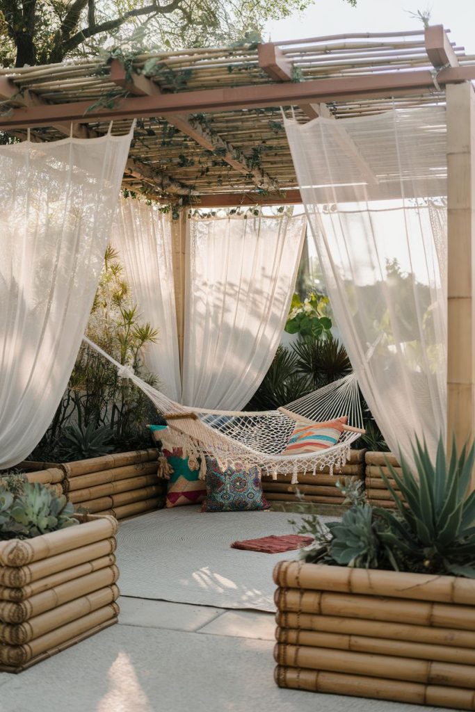 A hammock surrounded by sheer curtains and bamboo planters in a tranquil outdoor space under a wooden pergola.