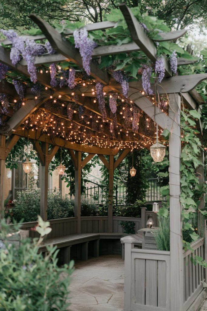 Wooden pavilion decorated with purple flowers and fairy lights surrounded by greenery.