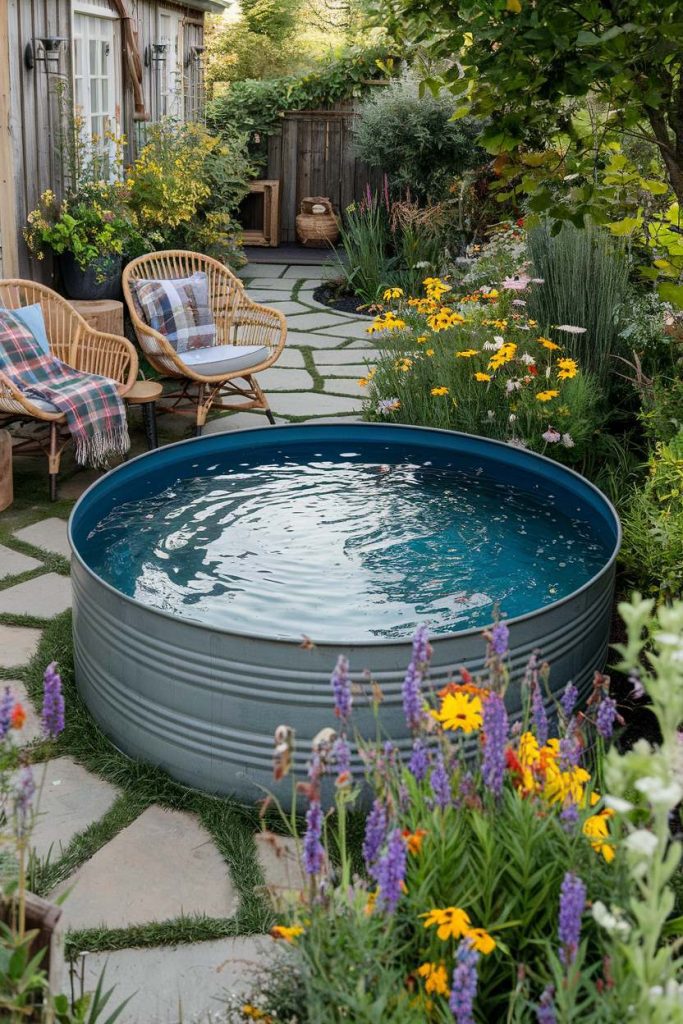 A tranquil garden setting with a round metal tank basin, wicker chairs and bright flowers.