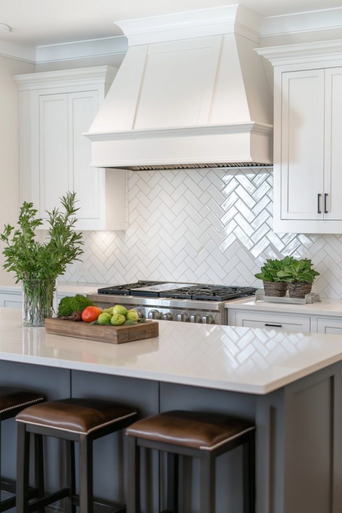 A modern kitchen with white cabinets, a herringbone tile backsplash and a center island with a white countertop and wooden stools. There are fresh herbs and vegetables on the counter.