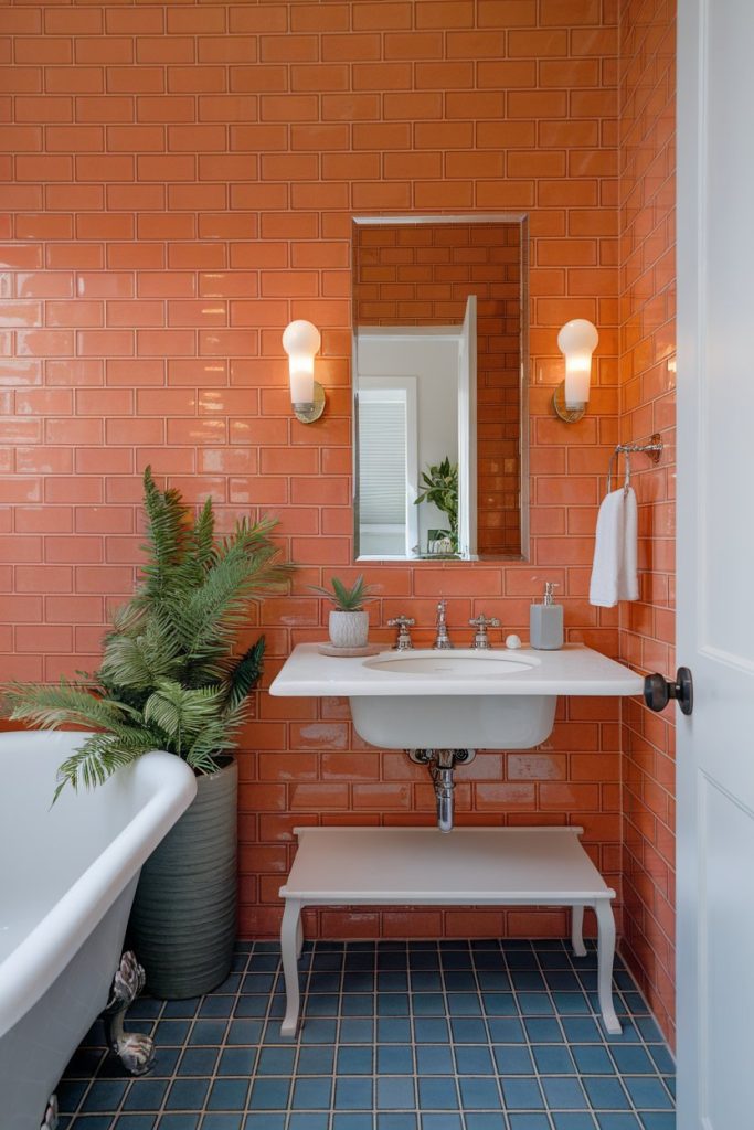 Bathroom with orange tiled walls, a white sink, wall lights, a mirror, plants in a green pot and a white freestanding bathtub on blue floor tiles.