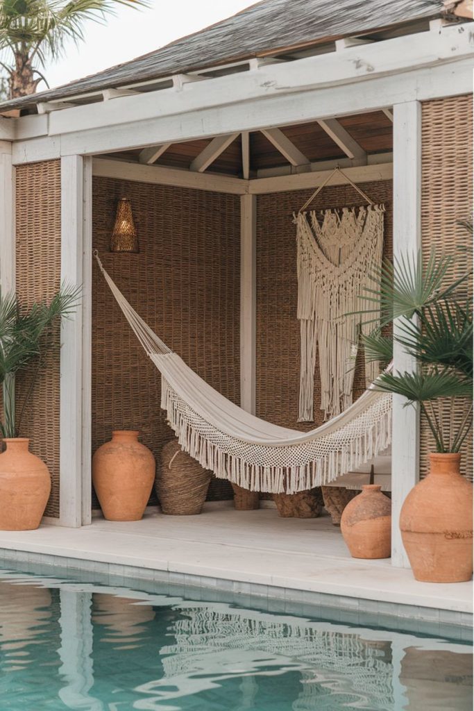 A cozy outdoor area with a white hammock surrounded by terracotta pots and palm plants, next to a pool.