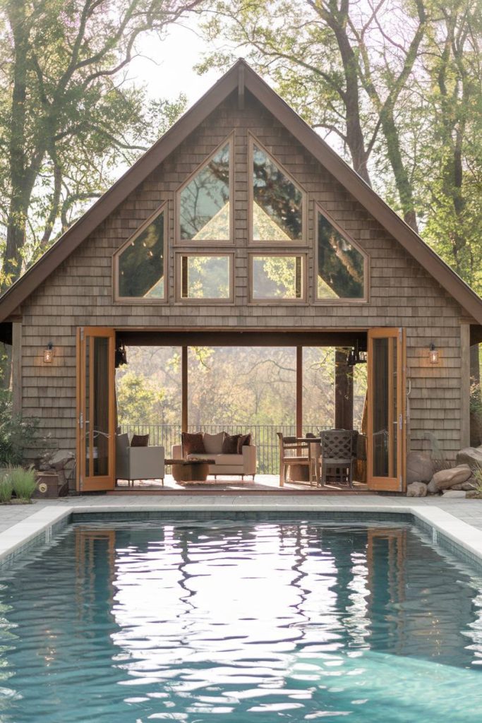 A-frame home with large windows and open doors overlooking a pool surrounded by trees.