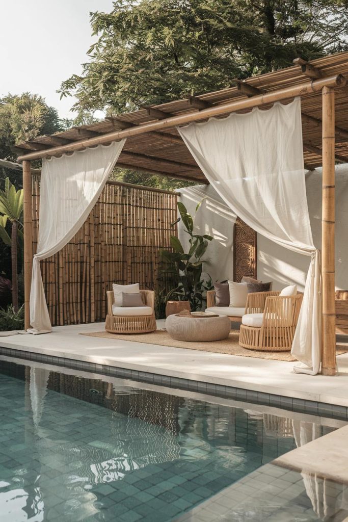 A tranquil poolside setting with a bamboo cabana, wicker furniture, white curtains and lush greenery.