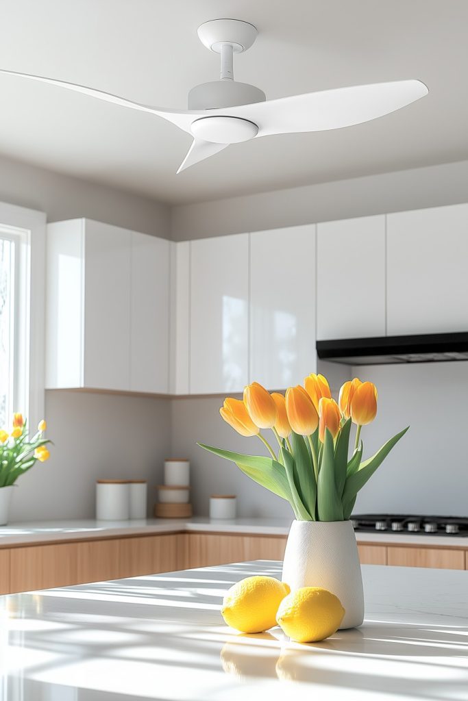 A modern kitchen with a white ceiling fan, glossy cabinets and a countertop with a vase of orange tulips and two lemons.