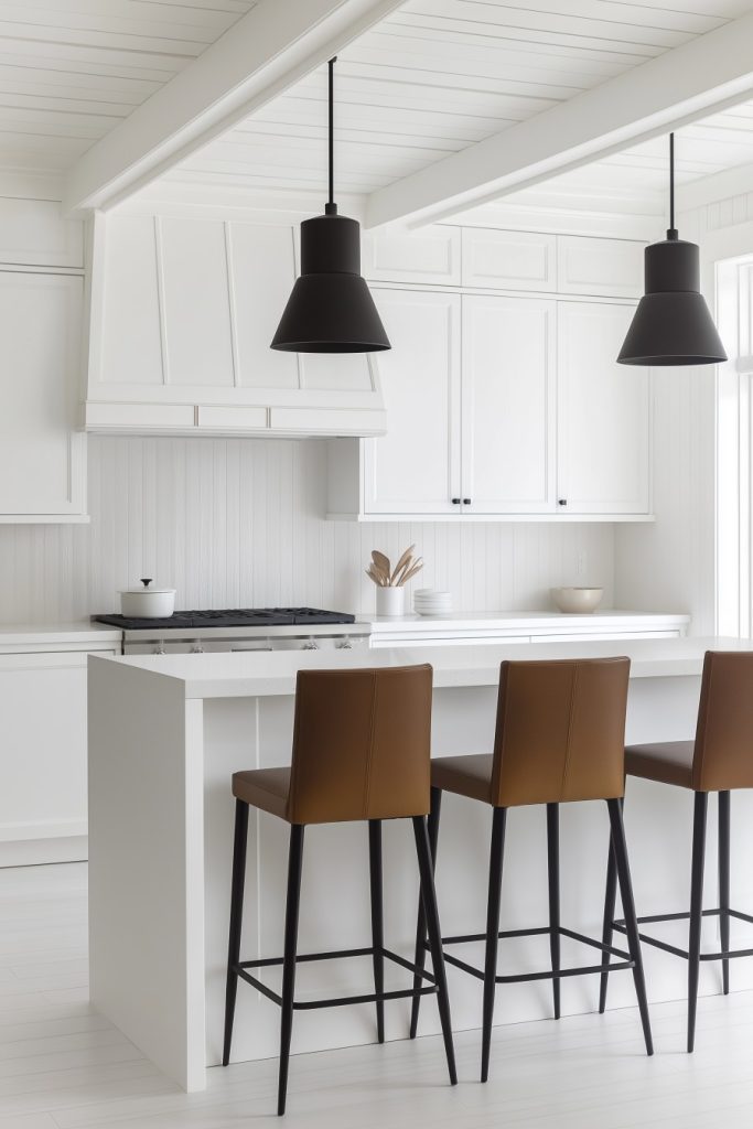 A modern kitchen with white cabinets, a white island and three brown bar stools. Two black pendant lights hang above the island.