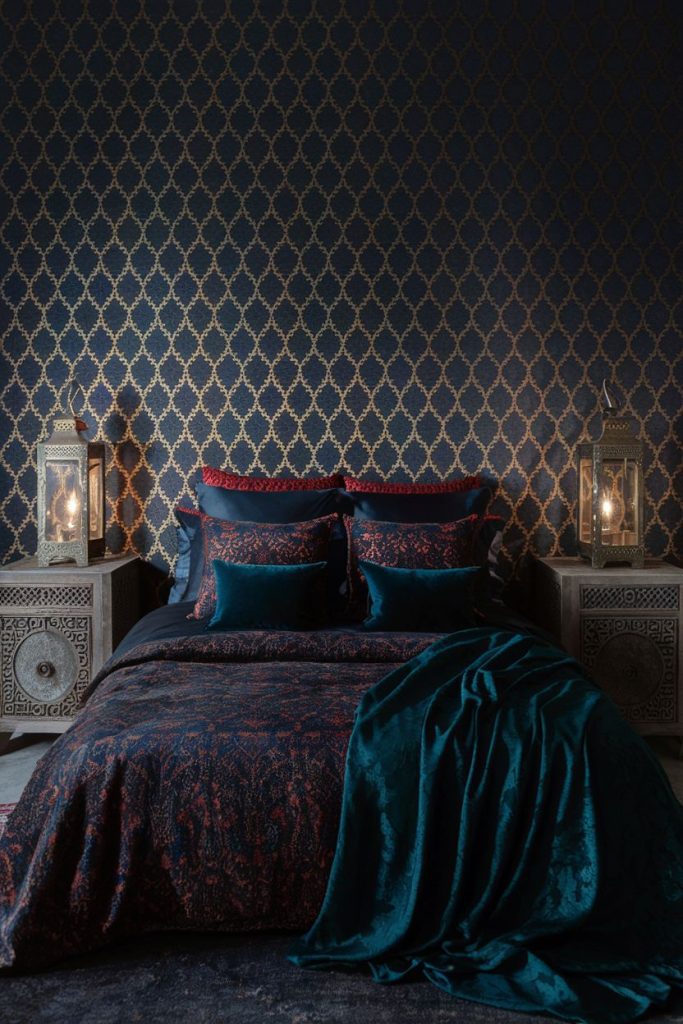 Luxury bedroom with dark blue and gold patterned wallpaper, a bed with dark blue and red linens and ornate lanterns on wooden bedside tables.