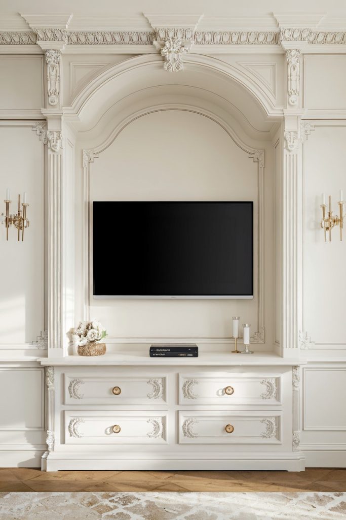 Elegant living room with a flat screen TV in a decorative alcove. Below are four drawers with ornate details and gold knobs, flanked by two sconces.