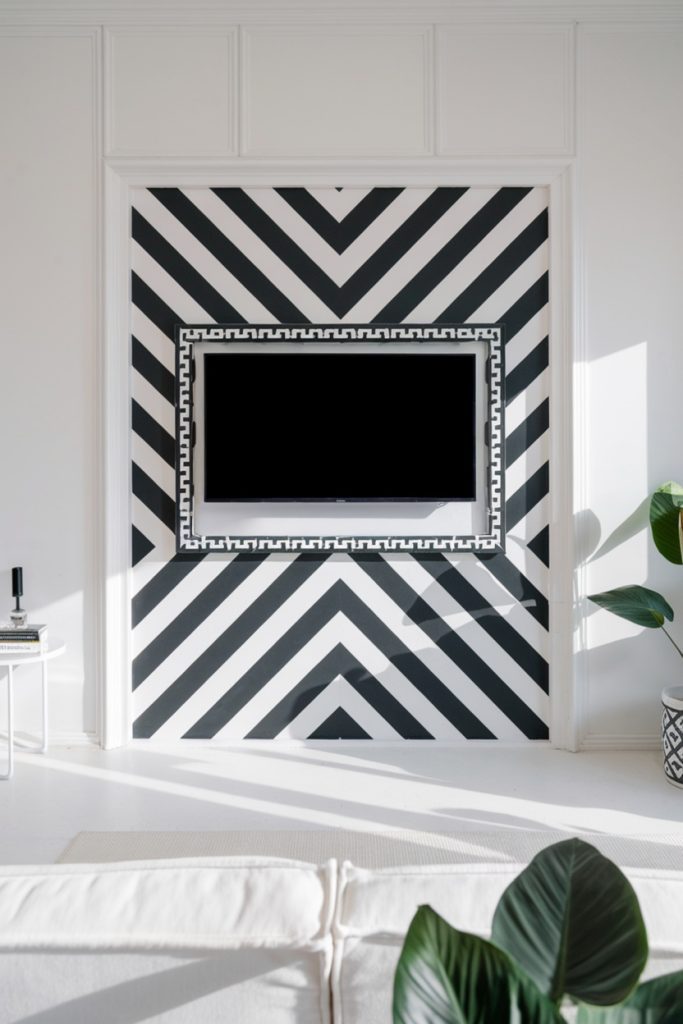 A wall-mounted television is set into a black-and-white, geometrically patterned wall. There is a white sofa in the foreground and a plant on the right.