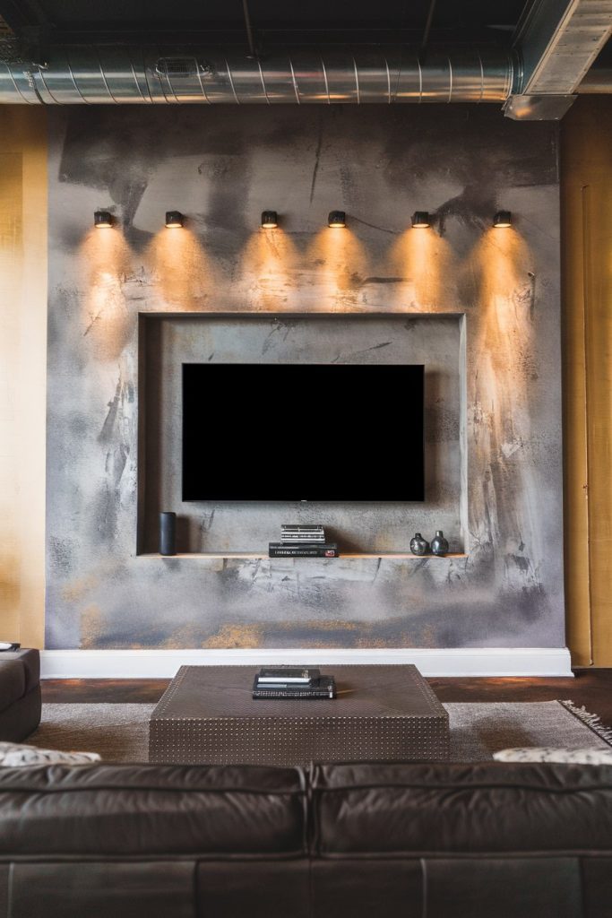 Modern living room with wall-mounted television, decorative lighting and a coffee table in front of a textured wall.