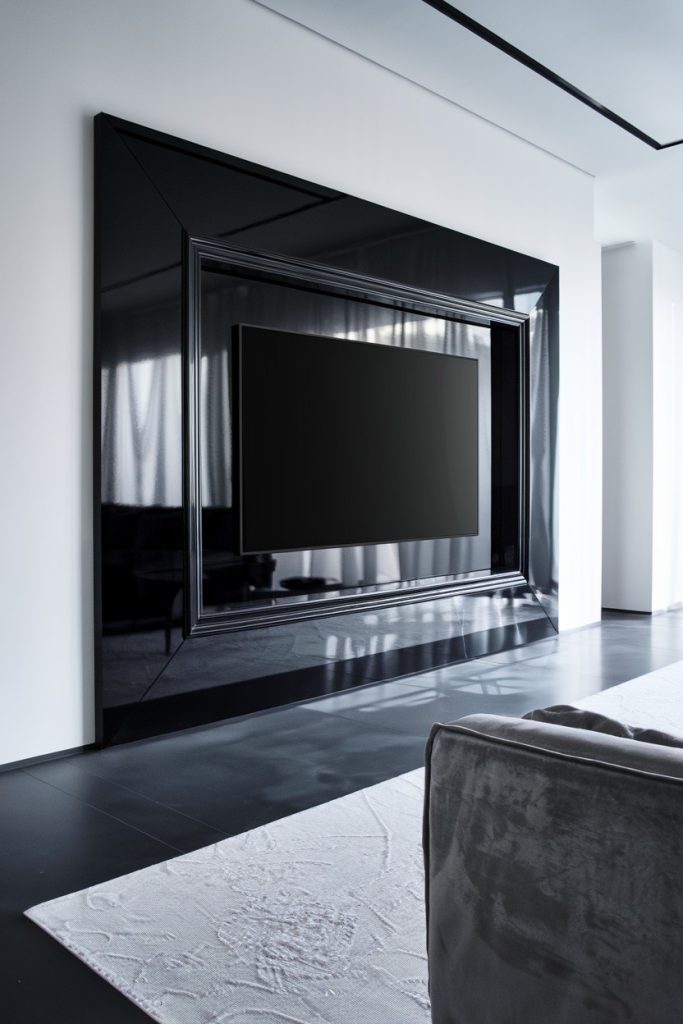 A minimalist living room features a large flat-screen TV on a glossy black wall with a white carpet and a gray sofa in the foreground.