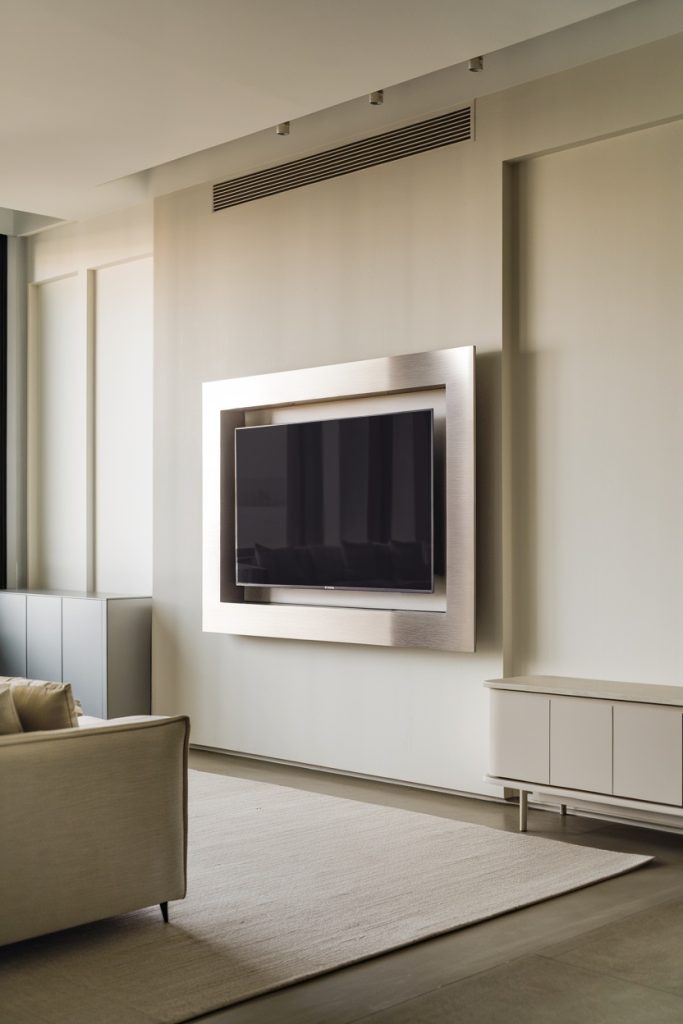 A modern living room with a sleek wall-mounted flat screen TV, a beige couch and a light rug.