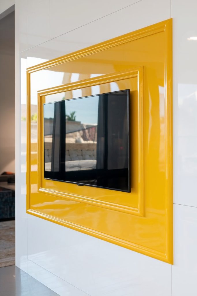 A flat-screen television is mounted on the wall, surrounded by a shiny yellow frame.