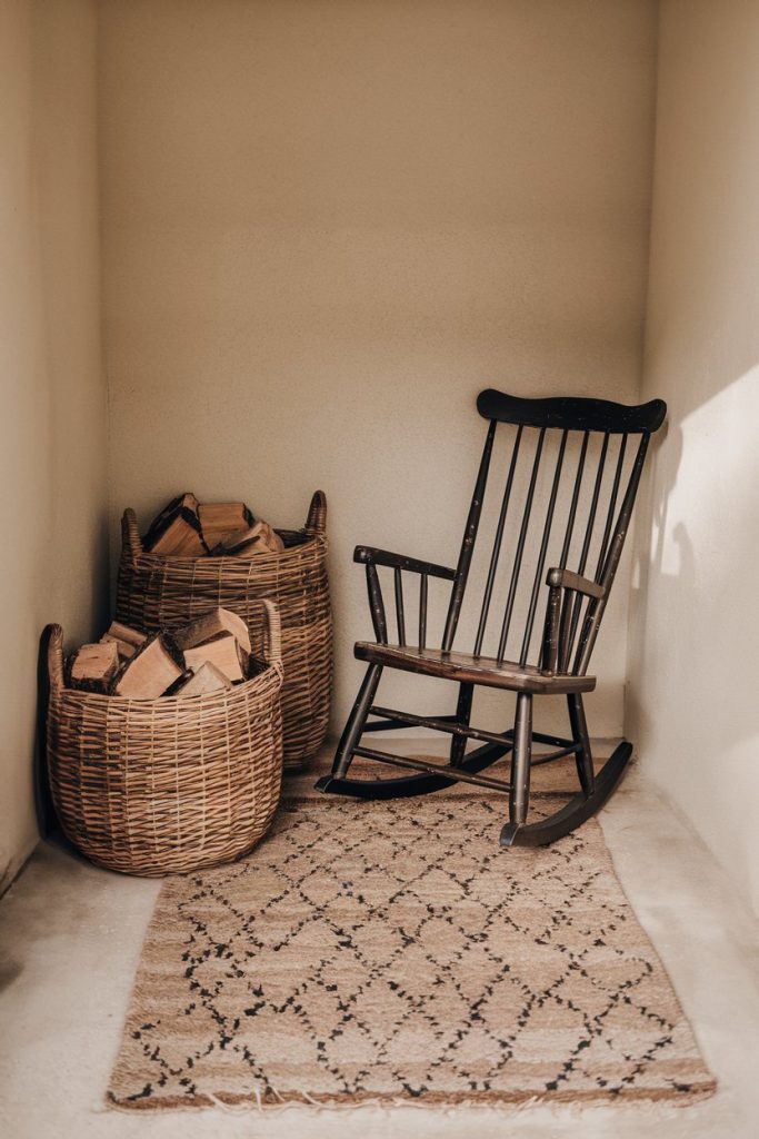 A rustic room with an antique rocking chair next to two baskets filled with firewood