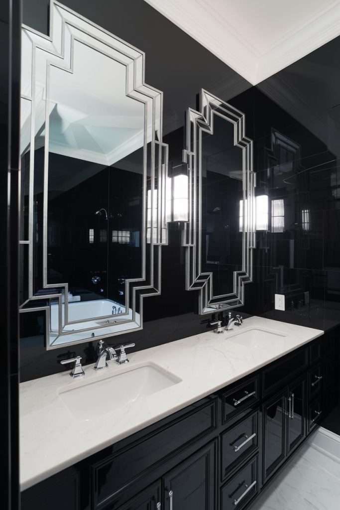 A modern bathroom with black walls, two geometric mirrors and a white countertop with double sinks and chrome faucets.