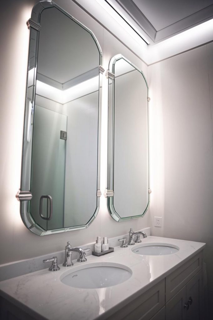 A modern bathroom vanity with two mirrors, two sinks and chrome faucets on a marble countertop.