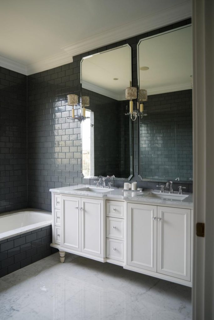 Bathroom with an elegant white vanity, large mirrors and dark tiled walls. A bathtub is placed to the side.