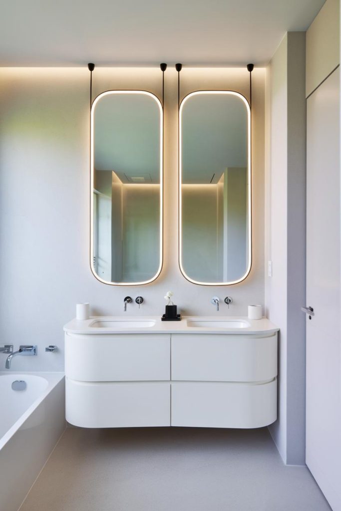 Modern bathroom with two oval mirrors above a double vanity, soft lighting and minimalist design.