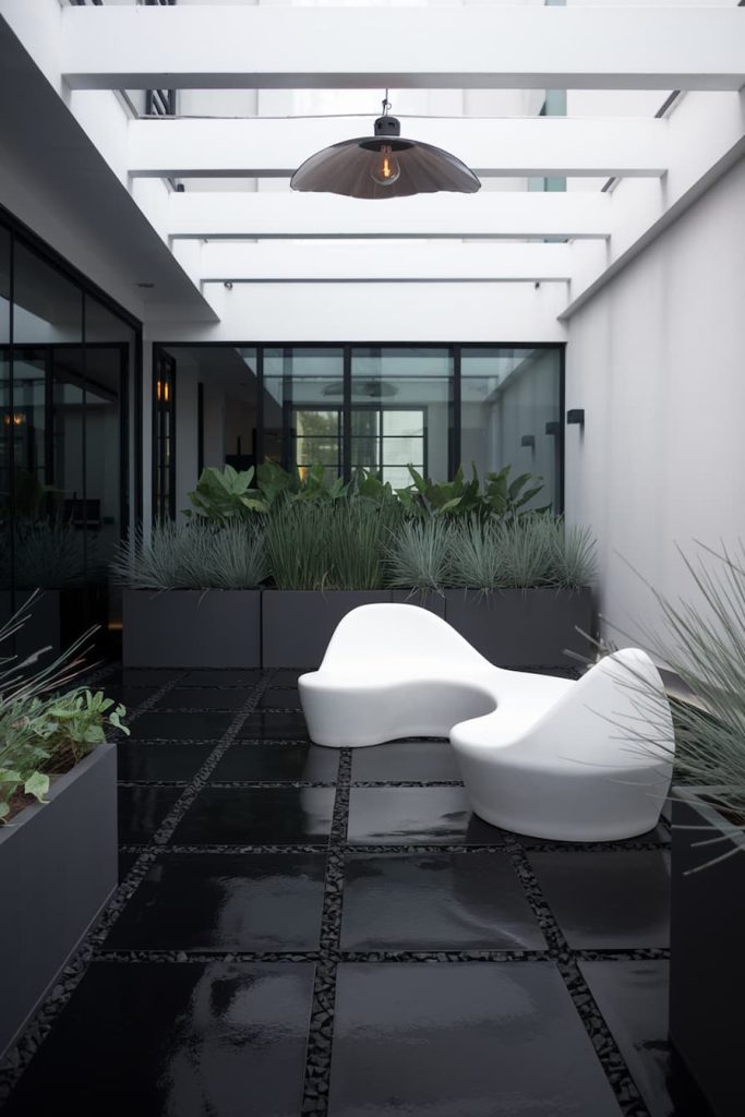 Modern interior patio with glossy black tiled floor, white sculpture chairs and planters with green plants. Above, a single black pendant light hangs from a white pergola.