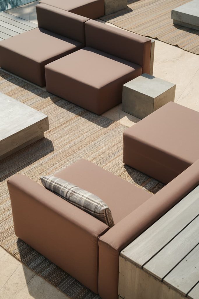 Modern outdoor seating with brown upholstered sofas and square concrete tables on a wooden terrace.