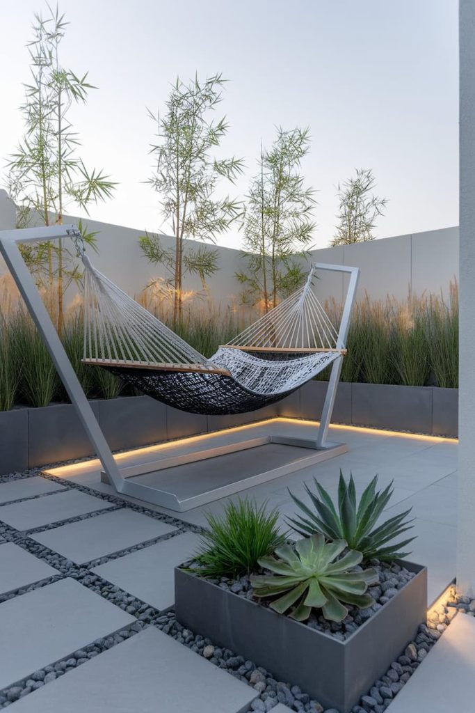 Modern outdoor patio with a hammock on a metal frame surrounded by decorative grasses, pavers and succulents in planters.