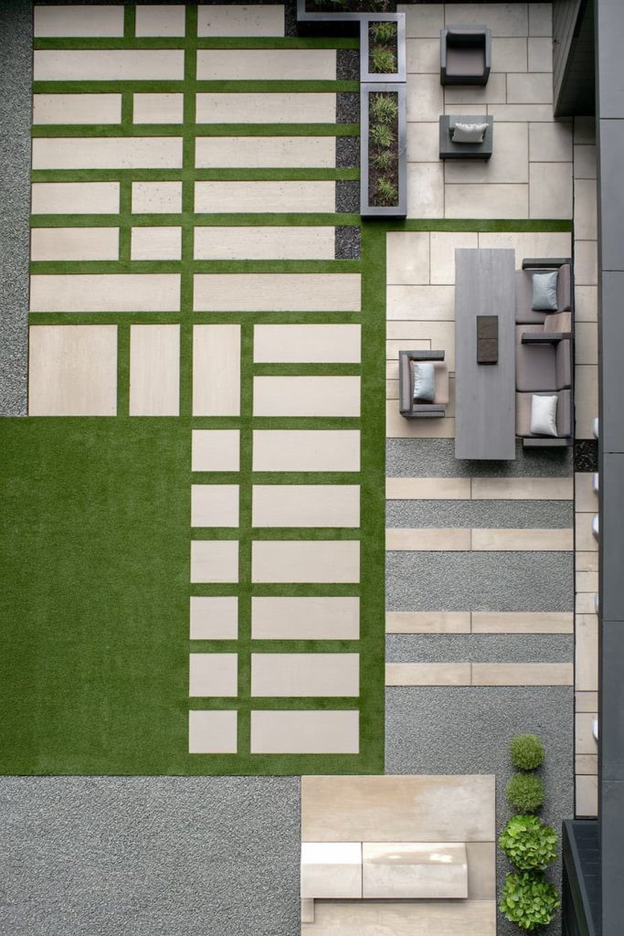 Aerial view of a modern patio with geometric stone tiles, artificial grass, a dining table with chairs and potted plants.