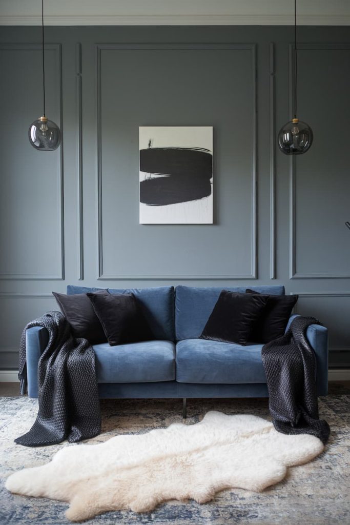 A modern living room with a blue sofa, black pillows, dark throws, an abstract black and white painting and hanging glass lamps. There is a fluffy white carpet on the floor.