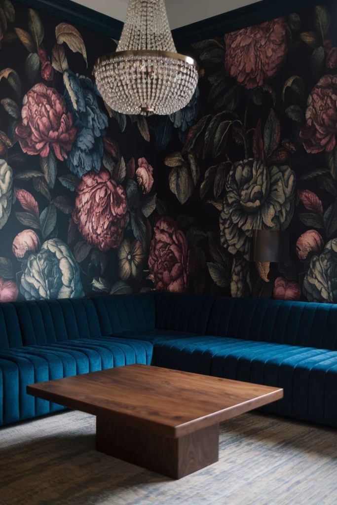 Room with dark floral wallpaper, a crystal chandelier, a blue velvet sofa set and a wooden coffee table.