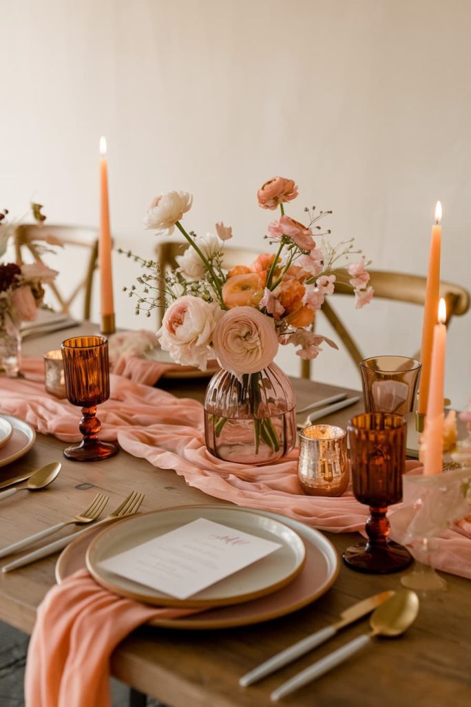 Elegant table setting with pink flowers, tall candles, amber glasses and a pink table runner. Two place settings with menus and gold cutlery.