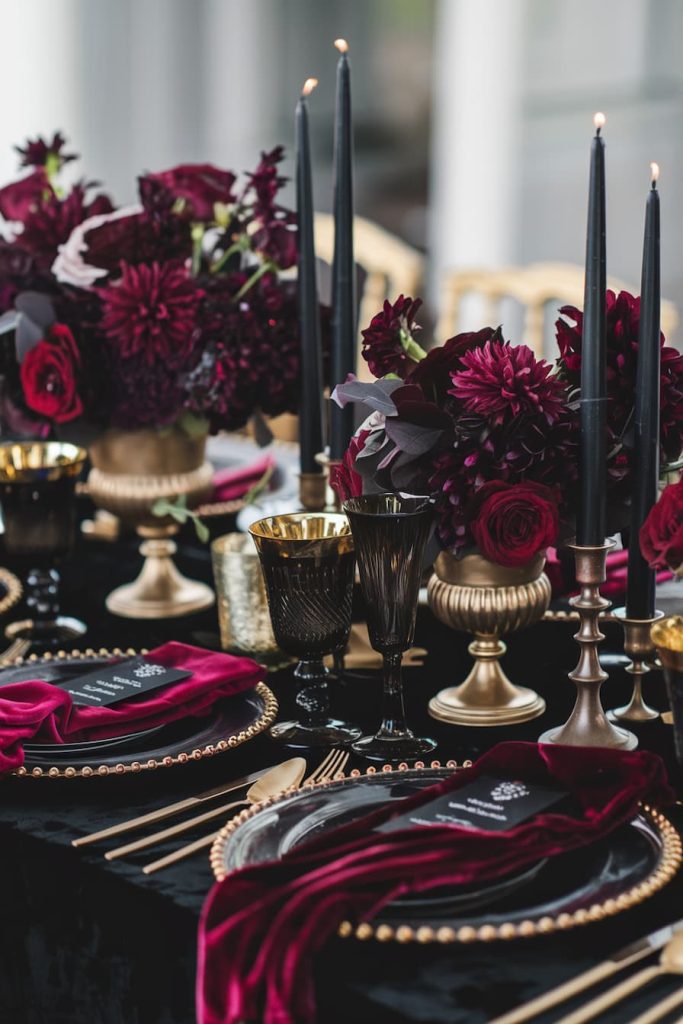 Elegant table setting with dark red flowers, black candles, gold accents and velvet napkins on a black tablecloth.