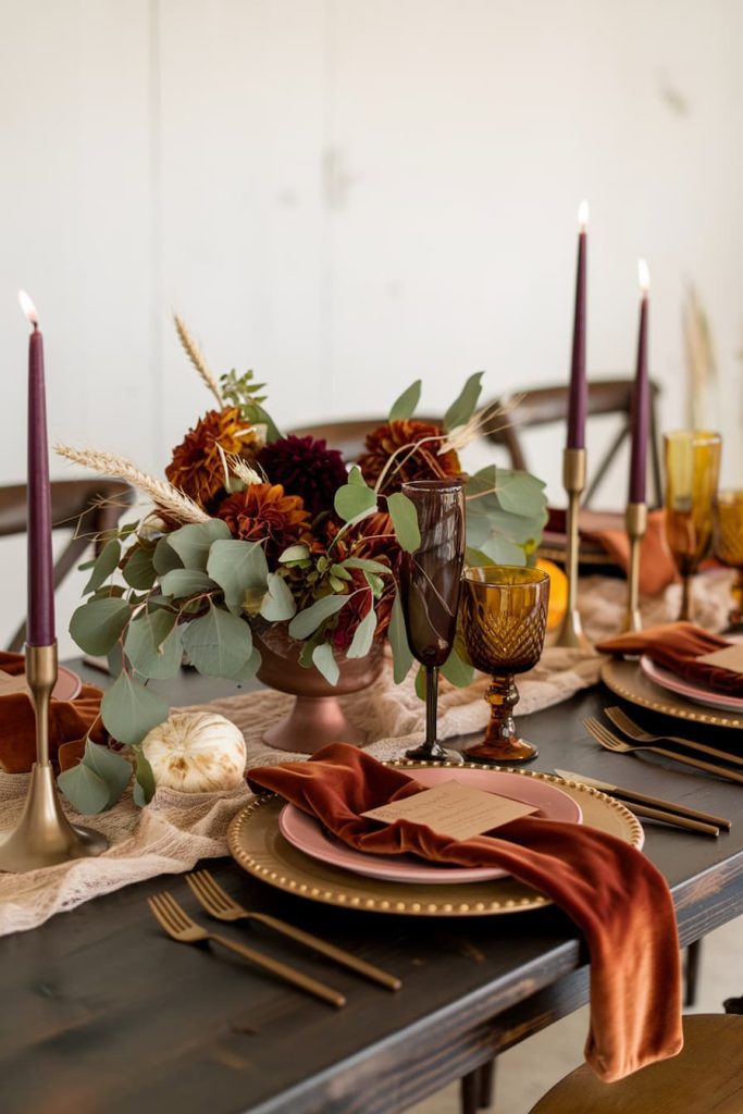 Elegant table decoration with autumn centerpiece with flowers and leaves. Candles, gold utensils and amber glasses complete the decoration on a dark wood table.