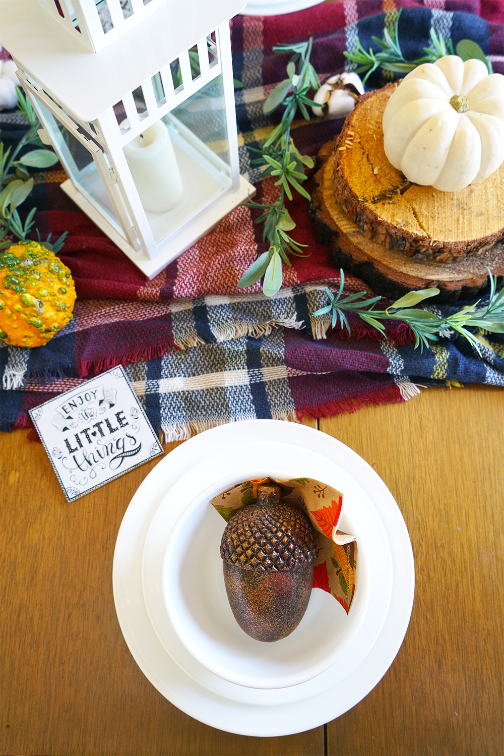 DIY fall tablescape with white Corelle dinnerware, plaid blanket, wood accents, and fall pumpkins.